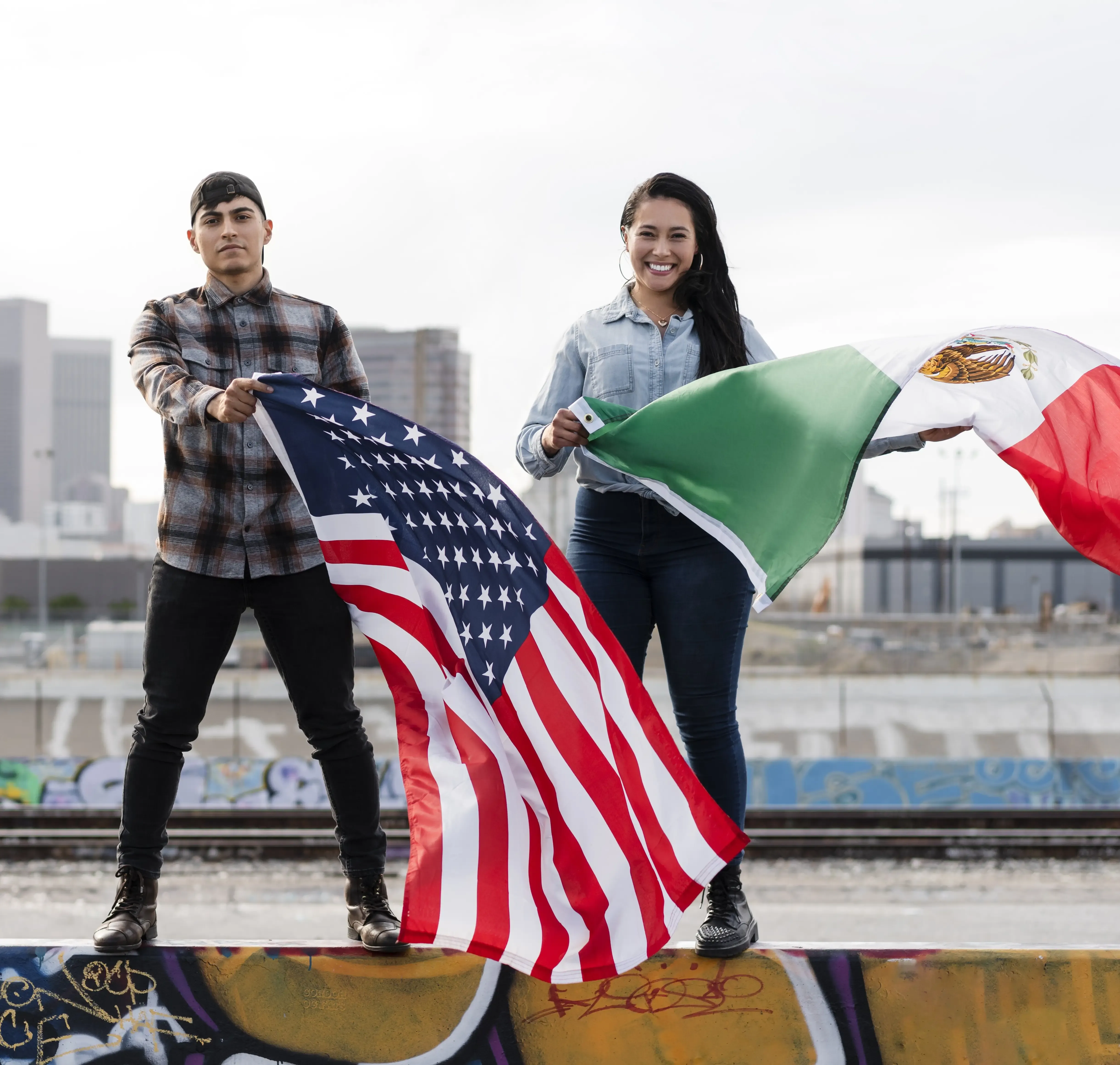 Un hombre y una mujer sosteniendo las banderas de Estados Unidos y México frente a un paisaje urbano, simbolizando el comercio bilateral.