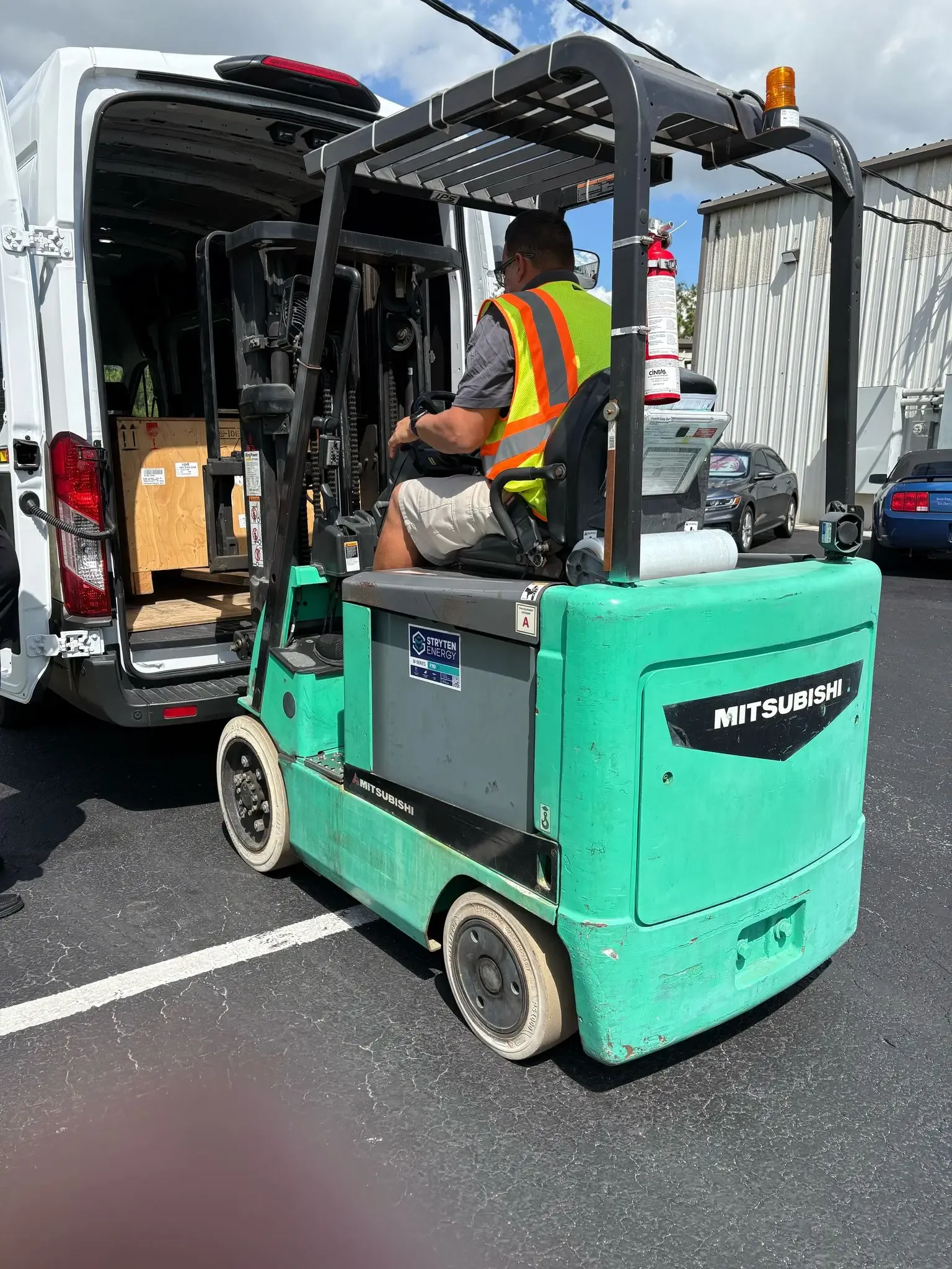 Forklift operator loading an export wooden crate into a white delivery van.