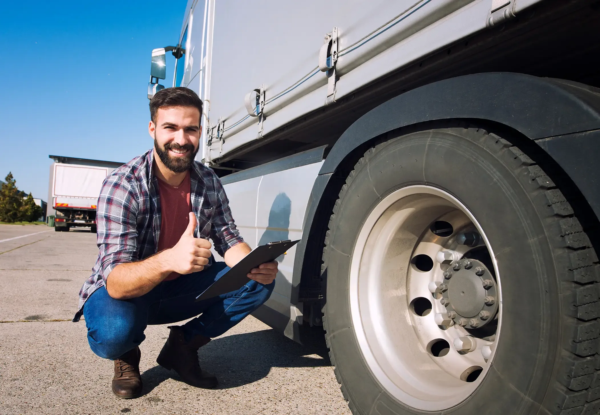 Worker smiling and making a thumbs-up gesture after checking truck tires.