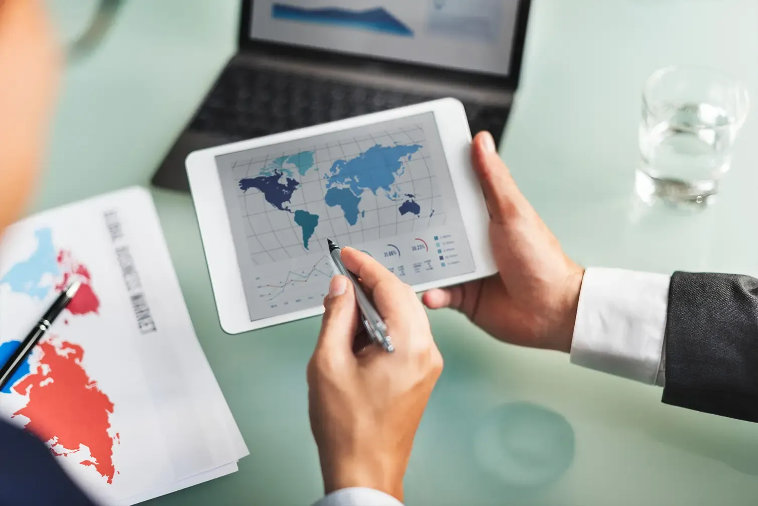 Business person analyzing a world map and growth charts on a tablet for import services.