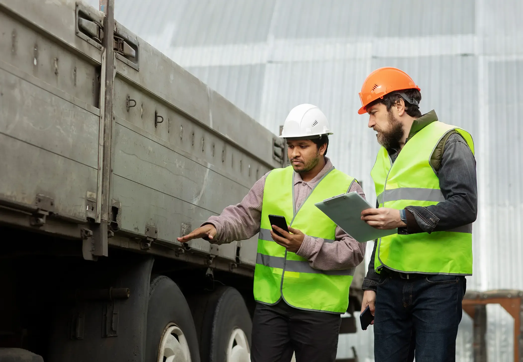Technical staff with safety vests performing a detailed inspection on the side of a cargo truck.
