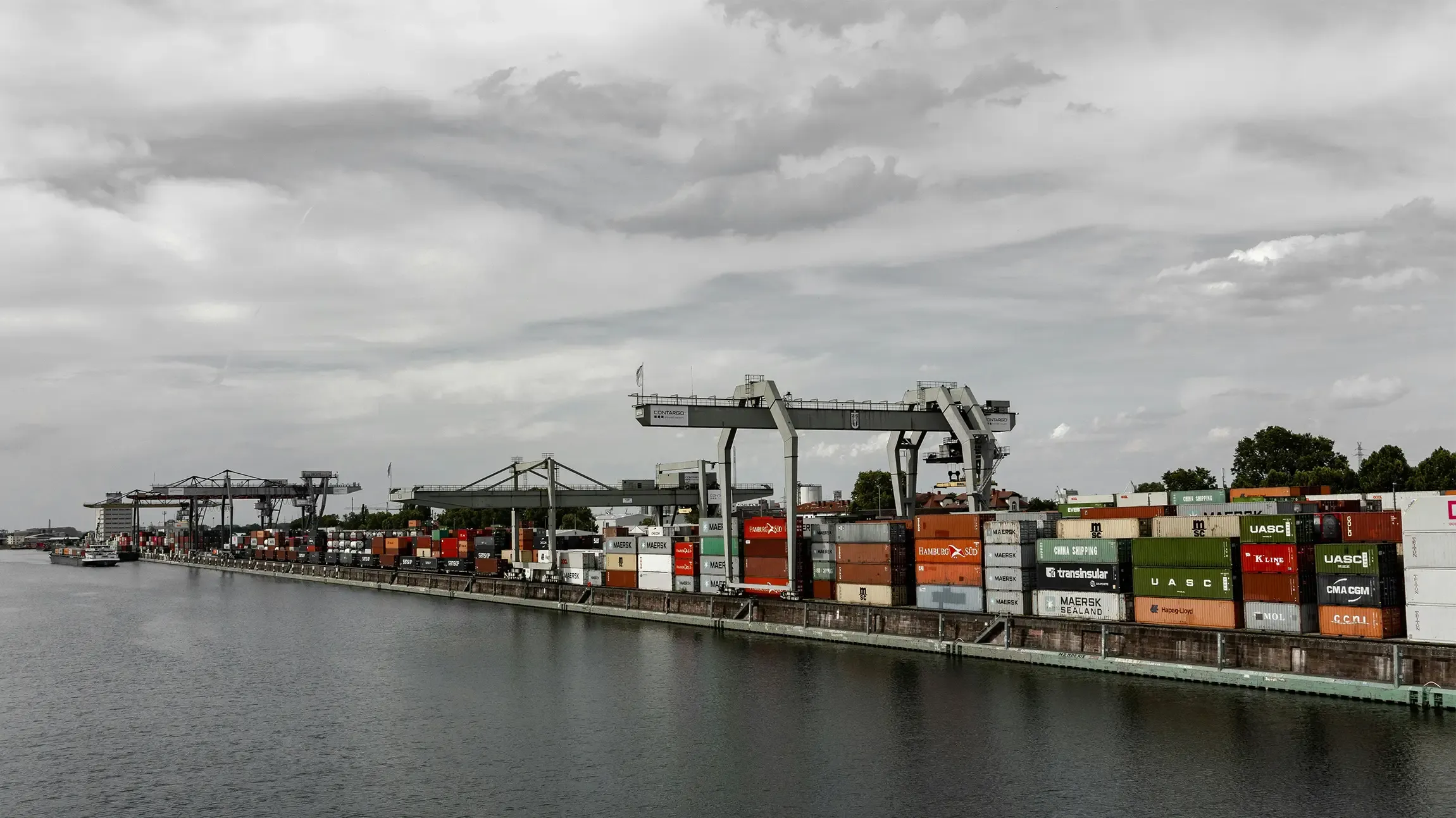 Orange gantry crane lifting a red container at a port cargo terminal.
