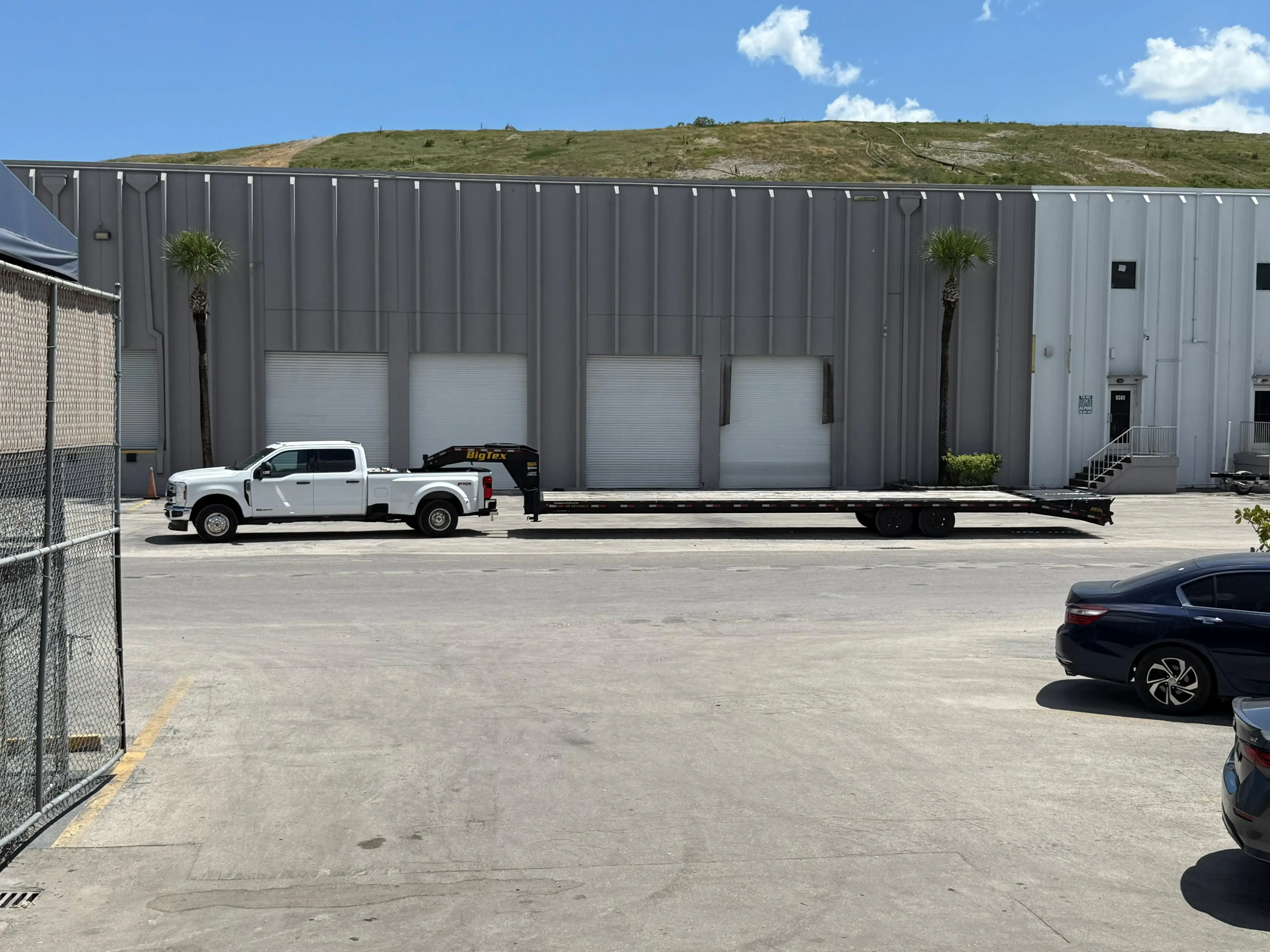 White Ford F-Series Super Duty truck with a Big Tex gooseneck flatbed trailer parked in a warehouse loading zone.
